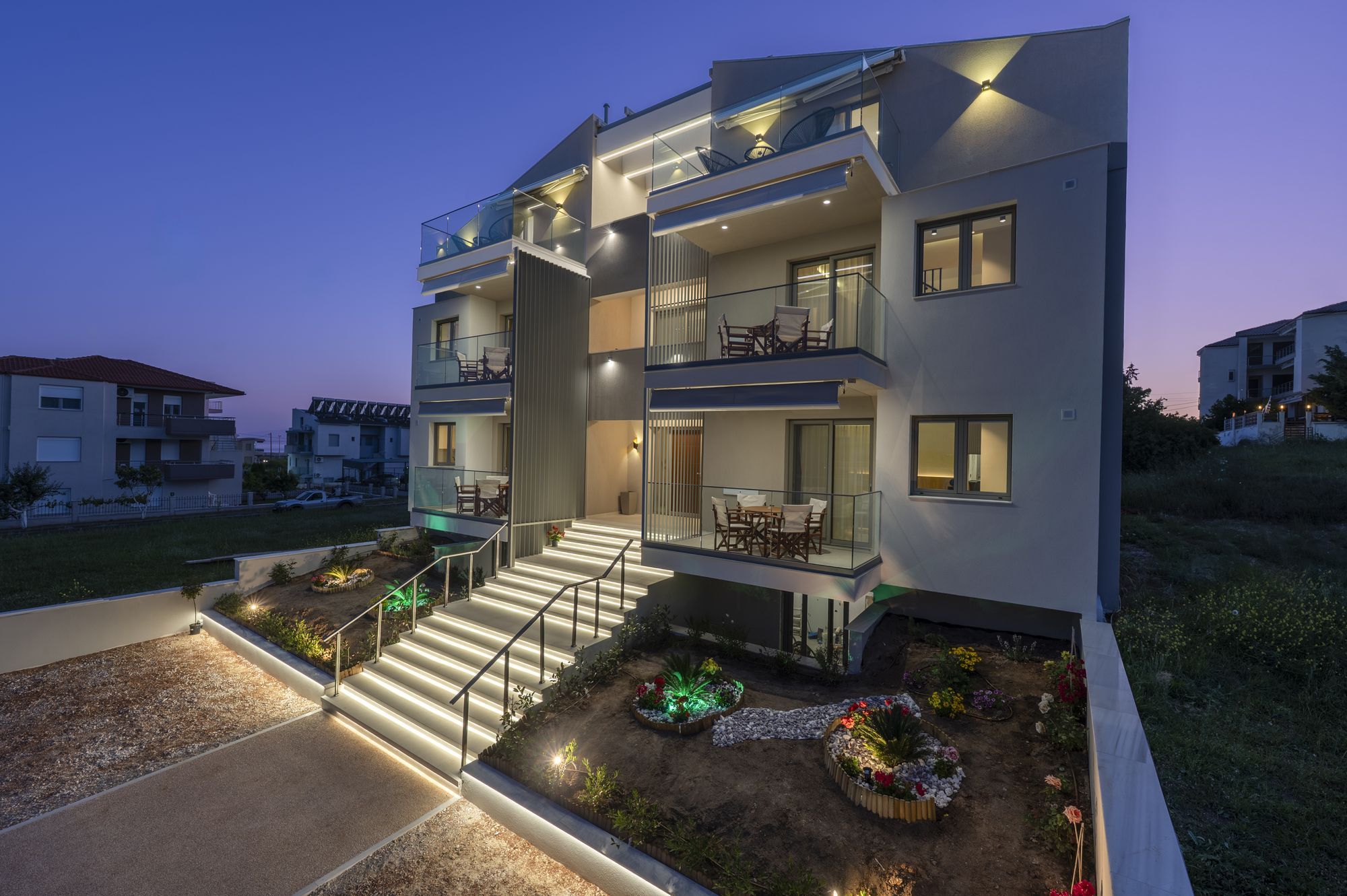 Το κτίριο Danae Luxurious Residences το σούρουπο, με φωτισμένη πρόσοψη, κήπο και σκάλες εισόδου